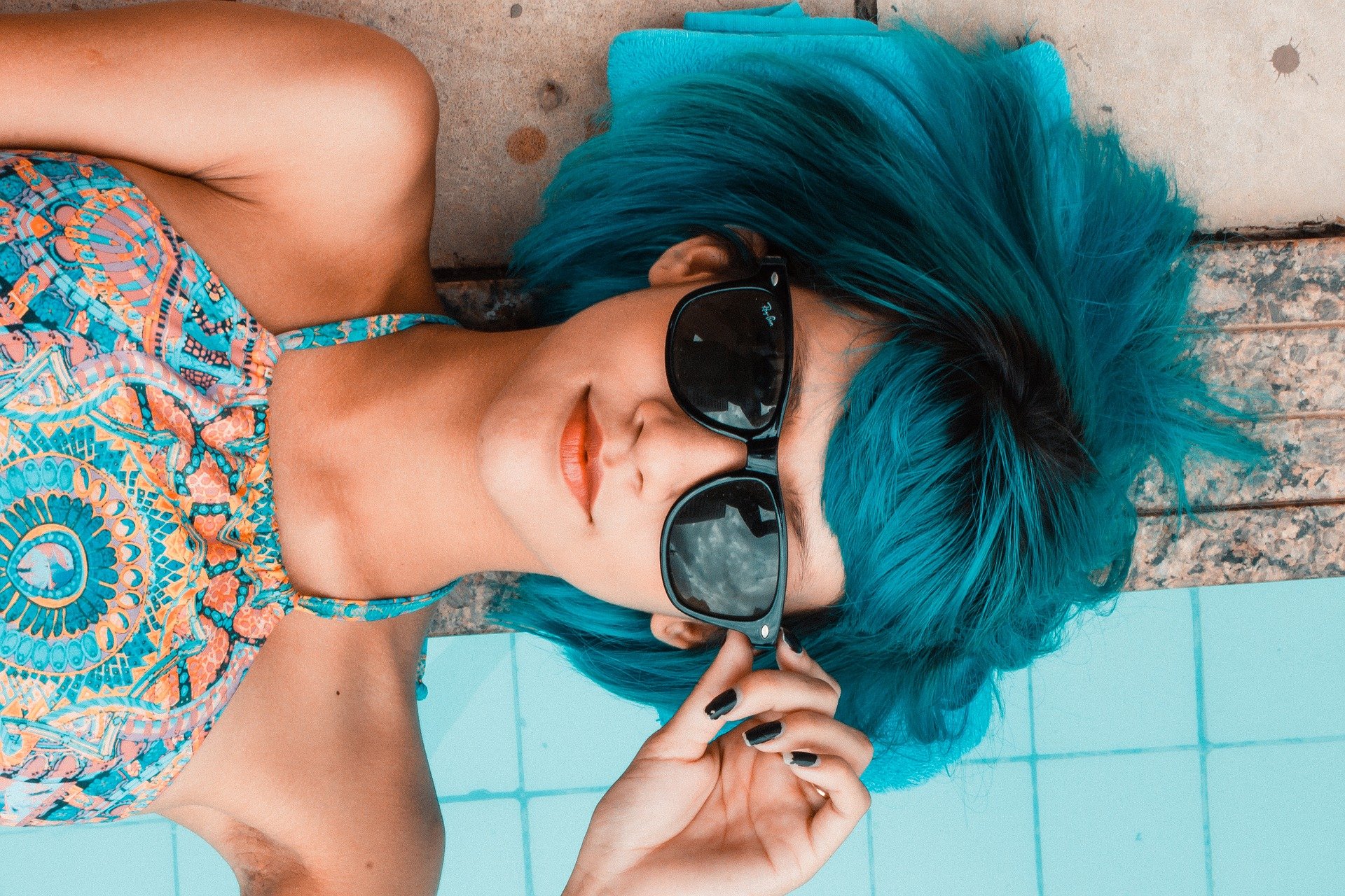 Mädchen mit blauen Haaren und Sonnenbrille liegt lässig auf dem Boden - Beitragsbild zum Thema: mit Kritik umgehen