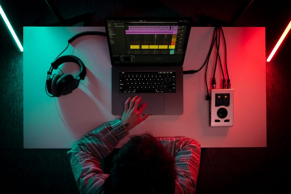 Mann sitzt vor Laptop und einer Musikproduktion