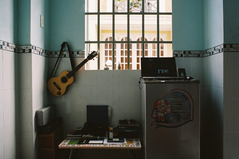 Gitarre hängt an Wand eines Zimmers im Retro-Stil. Auf Kühlschrank und Schreibtisch stehen Aufnahmegeräte.