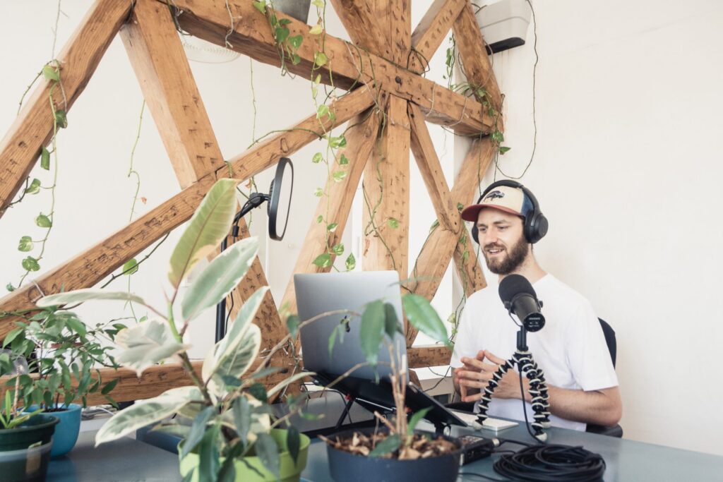 Ein Mann nimmt in seiner Wohnung einen Podcast am PC auf. Dabei nutzt er Podcast Apps.