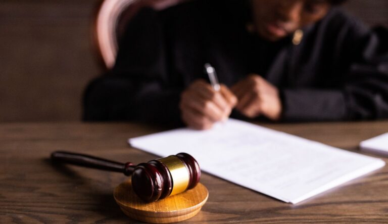 Eine Richterin schreibt auf ein Blatt Papier, vor ihr liegt ein Gerichtshammer