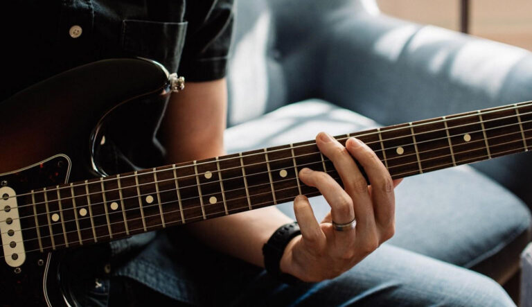 Das Bild zeigt eine Gitarre und ein junger Mann greift einen Dreiklang (triad) zum Thema: Die 4 Arten von Dreiklängen (Triads) + Umkehrungen auf der Gitarre